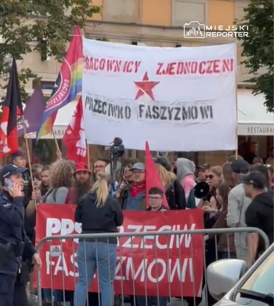 Grupa ludzi trzymająca transparenty i flagi w czasie protestu na ulicy, z hasłem "Przeciwko faszyzmowi".
