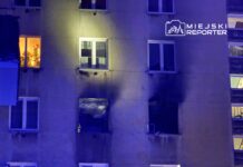 Na elewacji budynku widać okna, z których jedno jest oświetlone, a obok znajduje się okno z uszkodzeniami po pożarze.