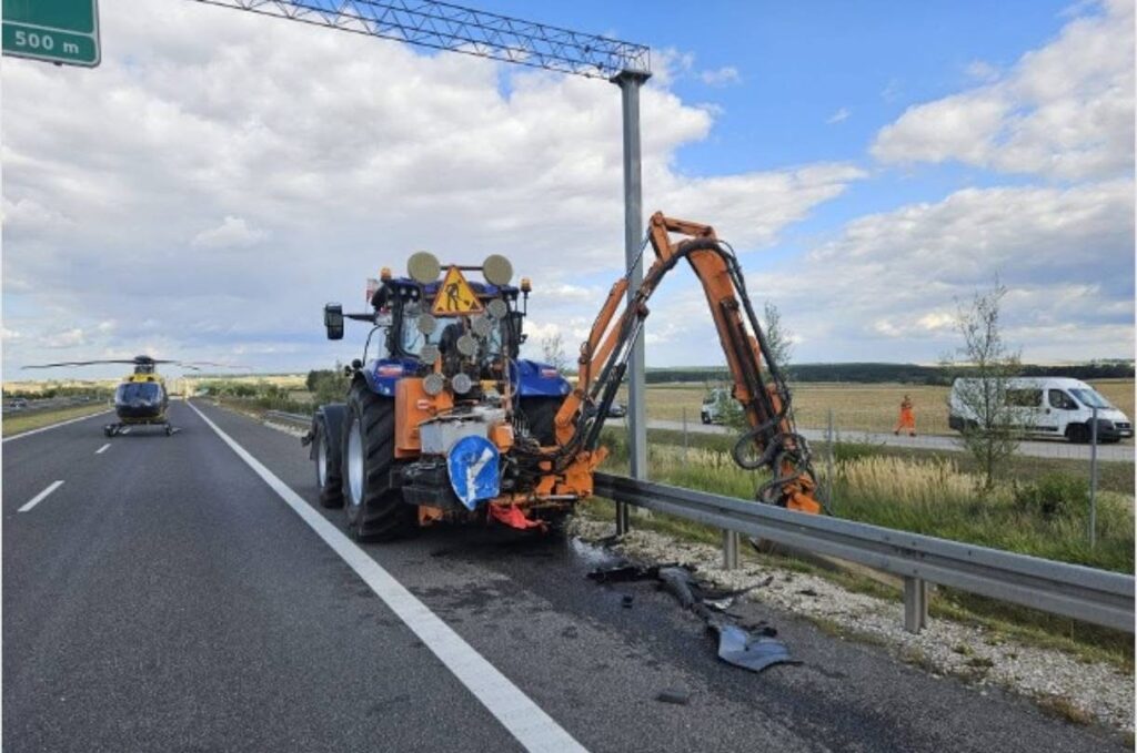 Traktor z urządzeniem do naprawy drogi pracuje przy barierkach na autostradzie, obok lądował śmigłowiec.