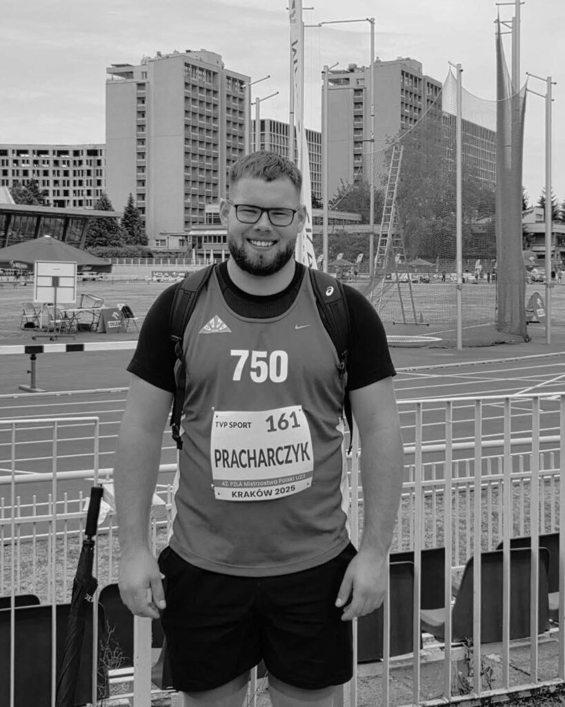 Mężczyzna w sportowym stroju z numerem startowym 750 stoi na tle stadionu lekkoatletycznego.