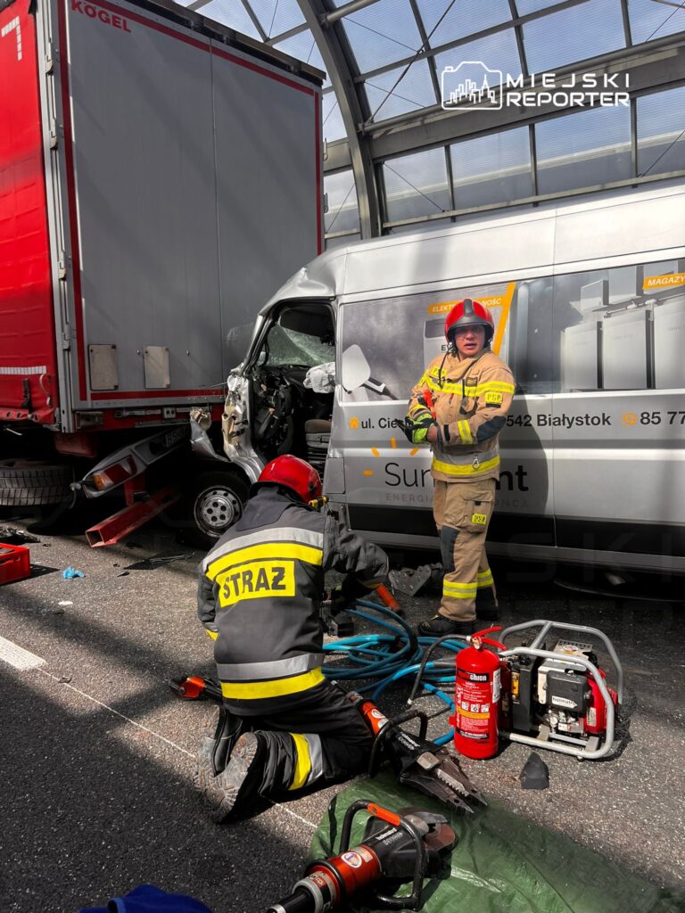 Strażacy w mundurach pracują przy wypadku drogowym, używając narzędzi hydraulicznych obok uszkodzonego pojazdu.