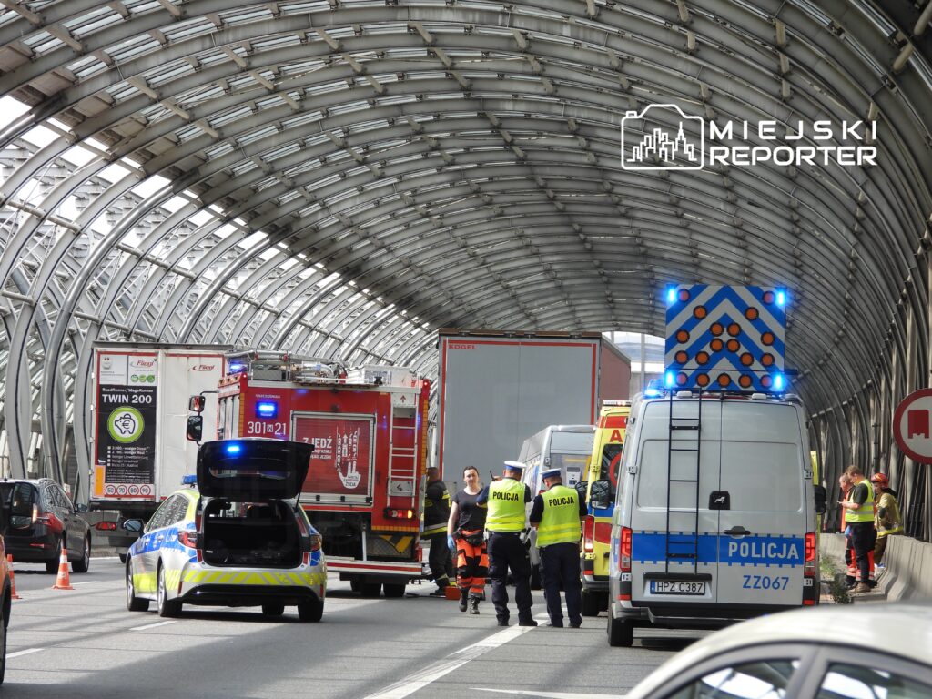 Grupa policjantów i strażaków pracuje na miejscu zdarzenia w tunelu drogowym, obok pojazdów ratunkowych.