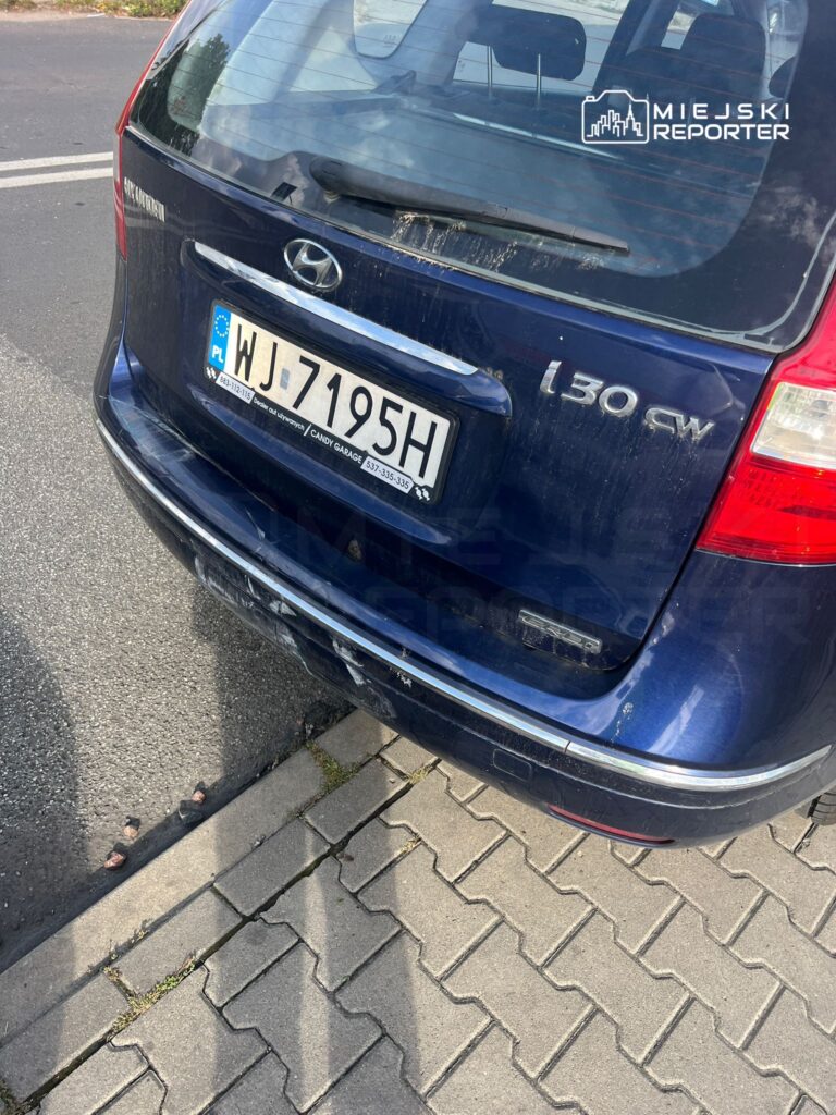 Czarny samochód marki Hyundai z widocznymi zarysowaniami zaparkowany na chodniku obok ulicy.