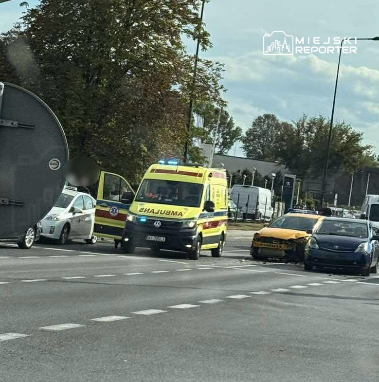 Karetka pogotowia z włączonymi sygnałami przy uszkodzonym samochodzie na ruchliwej drodze.