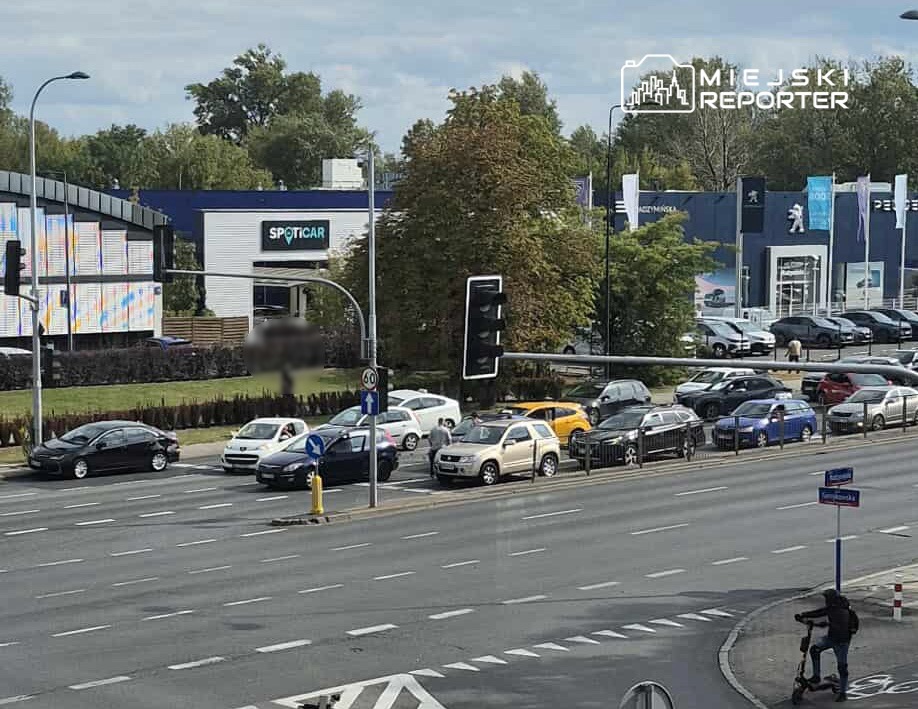Kierowca przestawia samochód na ruchliwej ulicy obok stacji dealerskiej z reklamą "SPOTICAR".
