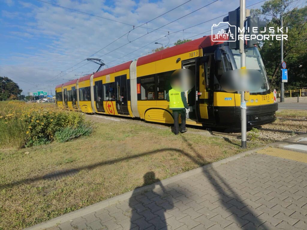 Tramwaj w żółto-czerwonym malowaniu stoi na przystanku, a pracownik w kamizelce podchodzi do drzwi.