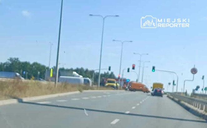 Ruch drogowy na skrzyżowaniu z sygnalizacją świetlną, widoczne ciężarówki i samochody osobowe.