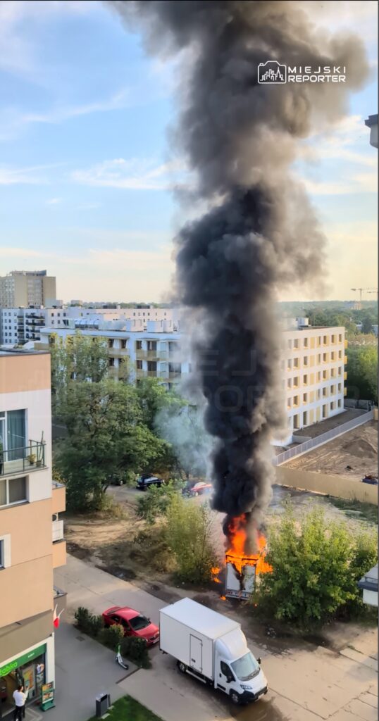 Pojazd dostawczy płonie w otoczeniu drzew, a z jego wnętrza wydobywa się gęsty, czarny dym.