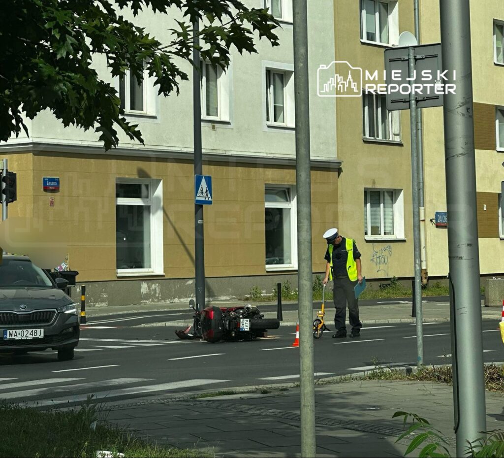 Policjant w kamizelce odblaskowej mierzy miejsce zdarzenia drogowego obok przewróconego motocykla na ulicy.