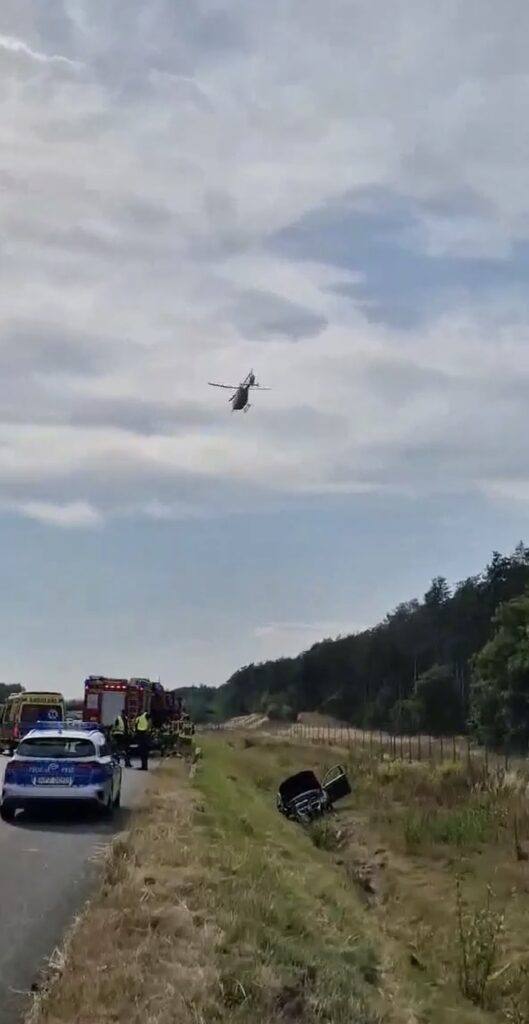 Helikopter ratunkowy przelatuje nad drogą, obok której trwa akcja ratunkowa po wypadku samochodowym.