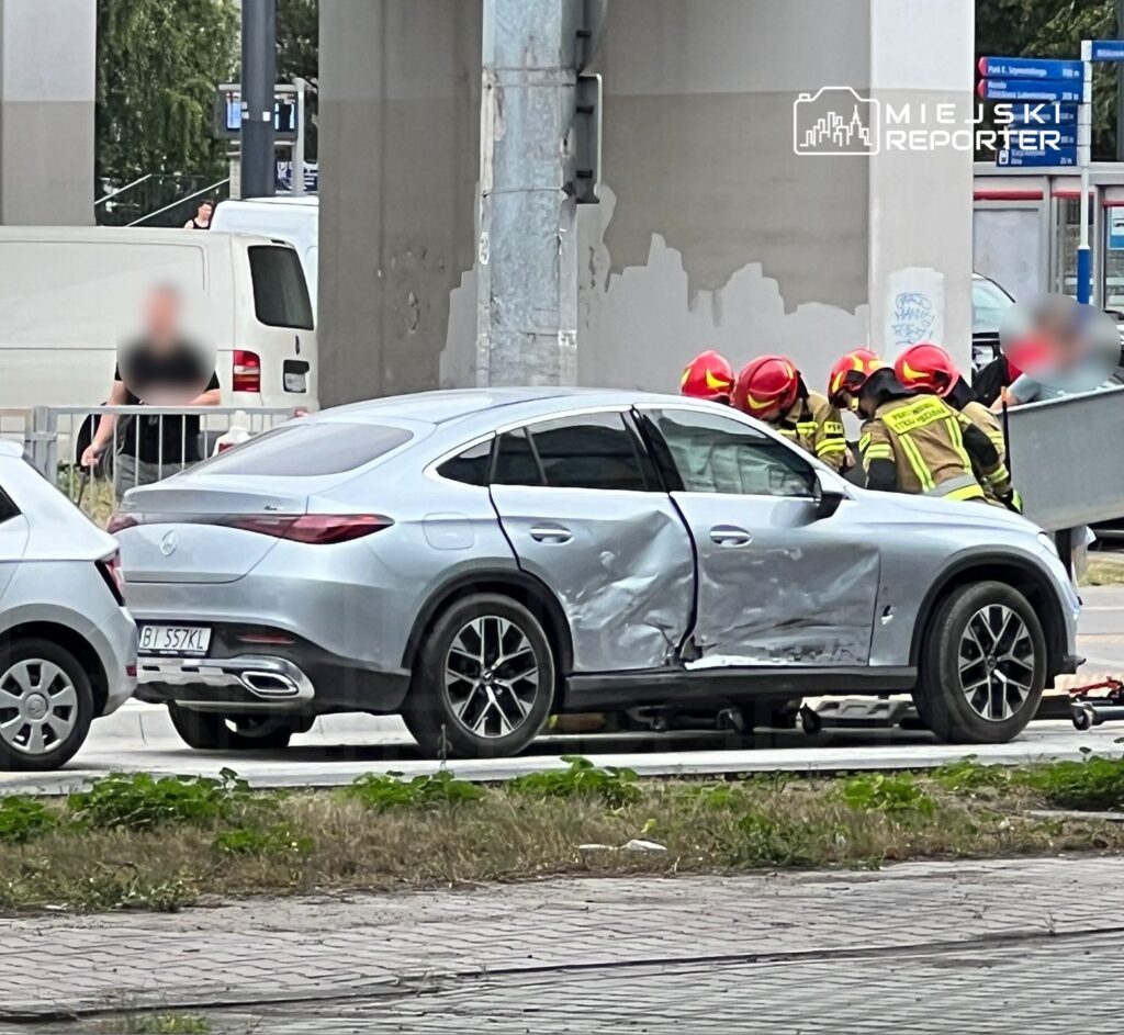 Zespół ratowników medycznych udziela pomocy poszkodowanemu przy uszkodzonym samochodzie w miejskim otoczeniu.