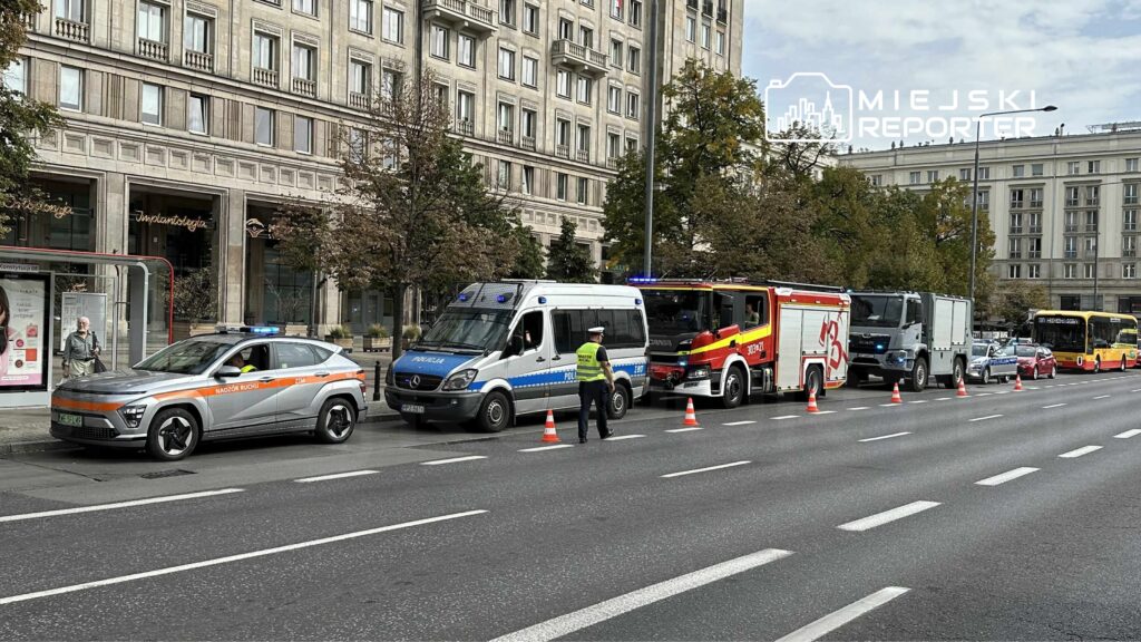 Pojazdy służb ratunkowych oraz policji stoją na ulicy, a funkcjonariusz kieruje ruchem w pobliżu przystanku.