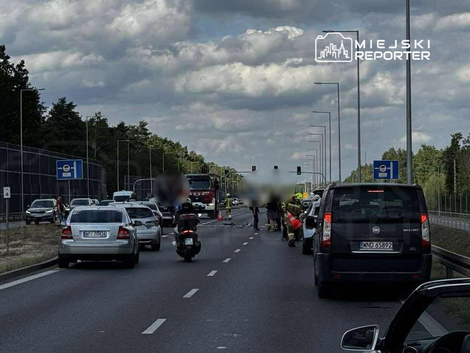 Na jezdni zatrzymane pojazdy, w tym samochód osobowy i motocykl, obok pracują służby ratunkowe.
