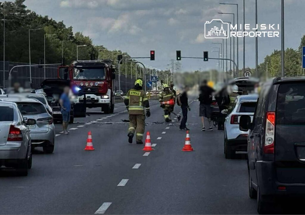 Strażacy zabezpieczają miejsce wypadku drogowego, podczas gdy kierowcy stoją obok swoich pojazdów na jezdni.