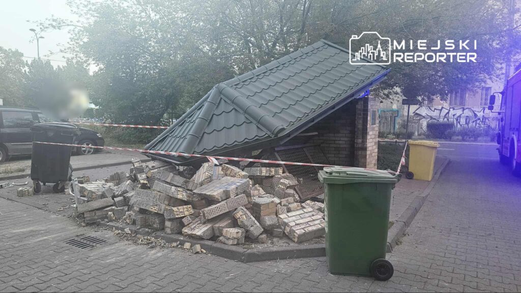 Zniszczona wiatka śmietnikowa z opadającym dachem, otoczona taśmą ostrzegawczą, obok dwa kontenery na odpady.