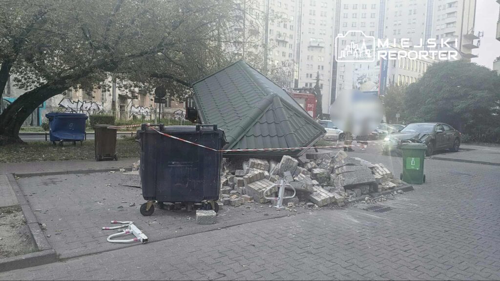 Zniszczona altanka ogrodowa leży na chodniku, otoczona gruzem i workami na śmieci, w tle bloki mieszkalne.