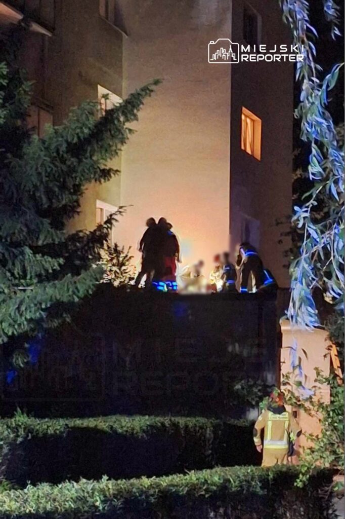 Grupa ratowników na dachu budynku, oświetlona reflektorami, w akcji ratunkowej po zmroku.