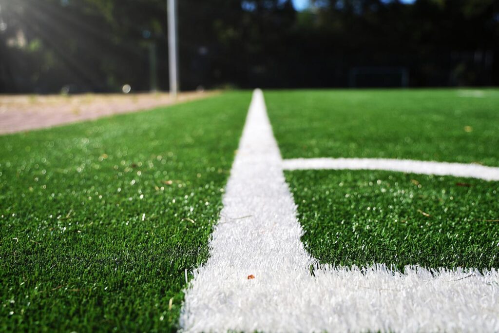 Widok na sztuczną murawę boiska sportowego z białą linią boczną w słonecznym otoczeniu.