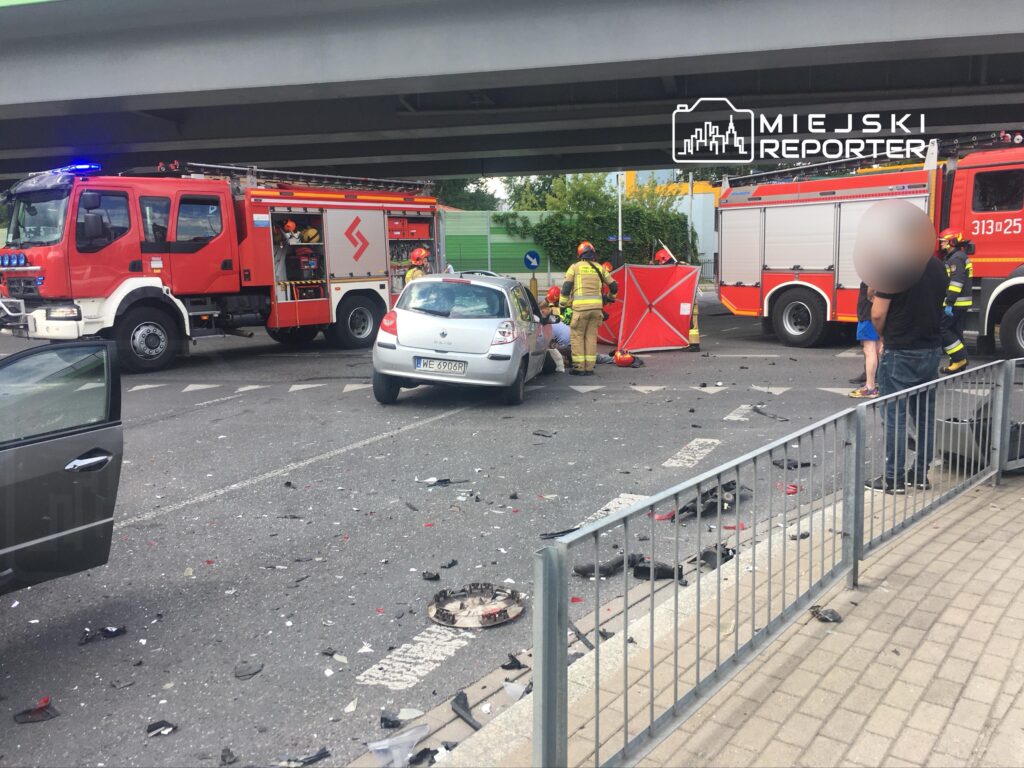 Strażacy udzielają pomocy poszkodowanemu w wypadku drogowym na zniszczonej jezdni, otoczeni wrakami pojazdów.