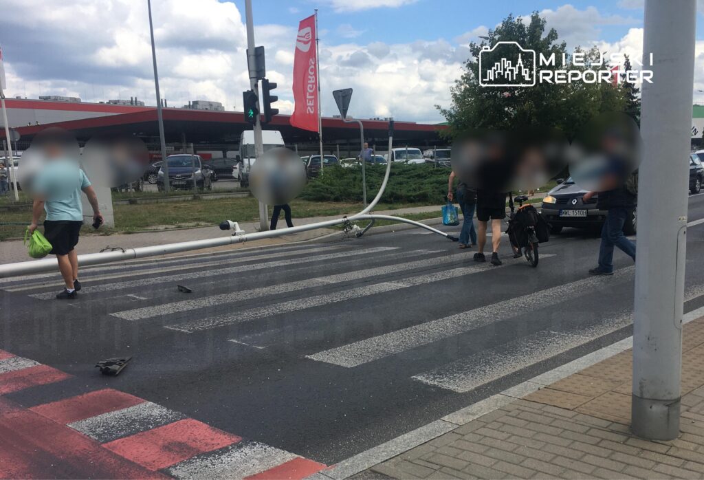 Grupa pieszych przechodzi przez pasy, obok leży uszkodzony element infrastruktury drogowej.