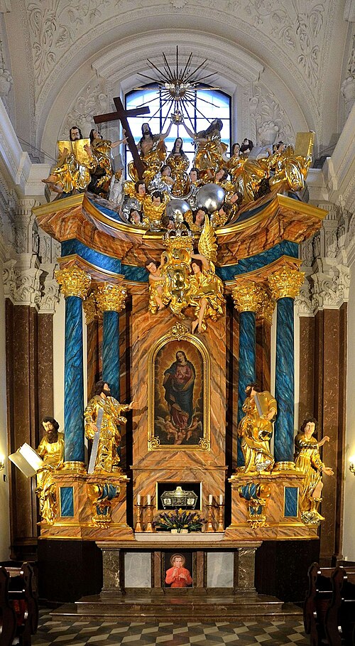 Ołtarz z bogato zdobionymi figurami świętych i aniołów, z centralnym obrazem Madonny, w jasnym wnętrzu kościoła.