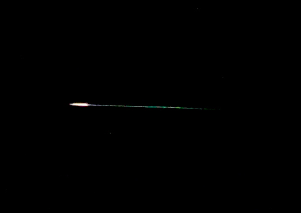 Meteor przelatujący przez nocne niebo, emitujący jasne światło i kolorowy ogon.