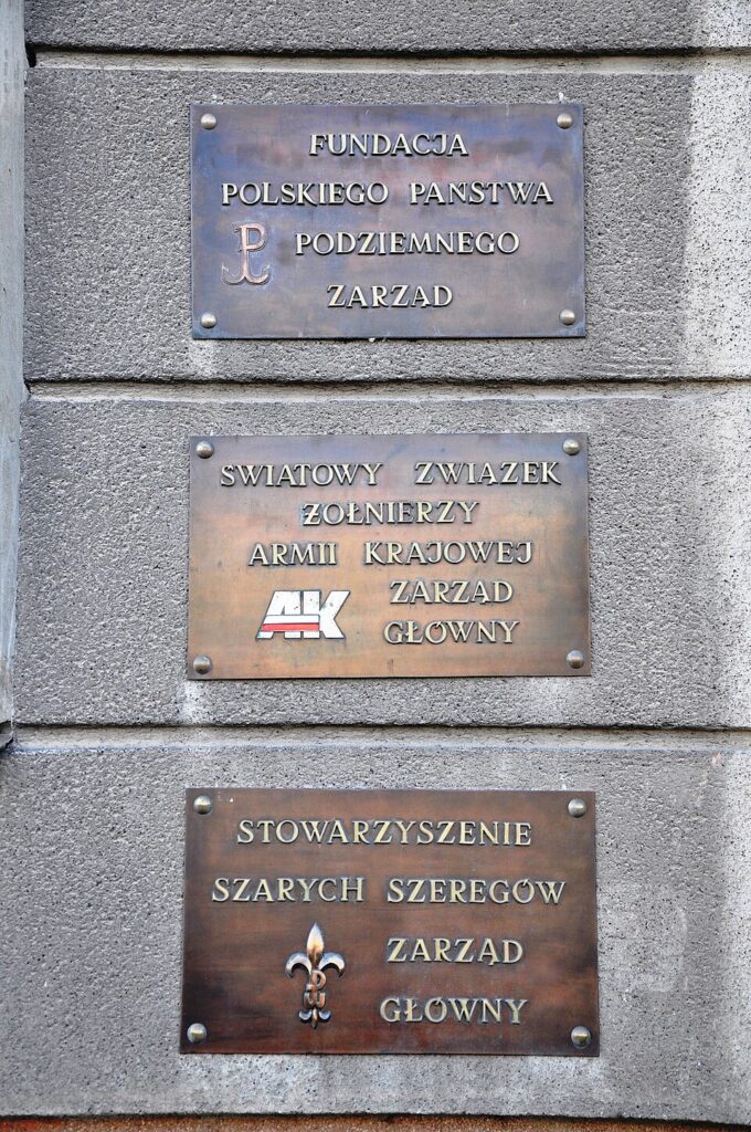 Tablice z nazwami organizacji umieszczone na szarej ścianie budynku, w tym "Fundacja Polskiego Państwa Podziemnego" oraz "Światowy Związek Żołnierzy Armii Krajowej".