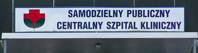 Tablica informacyjna z napisem "SAMODZIELNY PUBLICZNY CENTRALNY SZPITAL KLINICZNY" umieszczona na budynku szpitala.