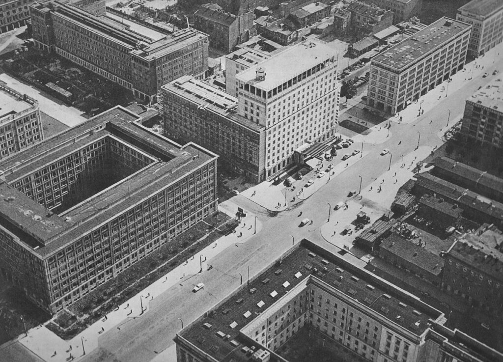 Widok z lotu ptaka na miejską architekturę, w tym nowoczesne budynki i ulice z samochodami oraz pieszymi.