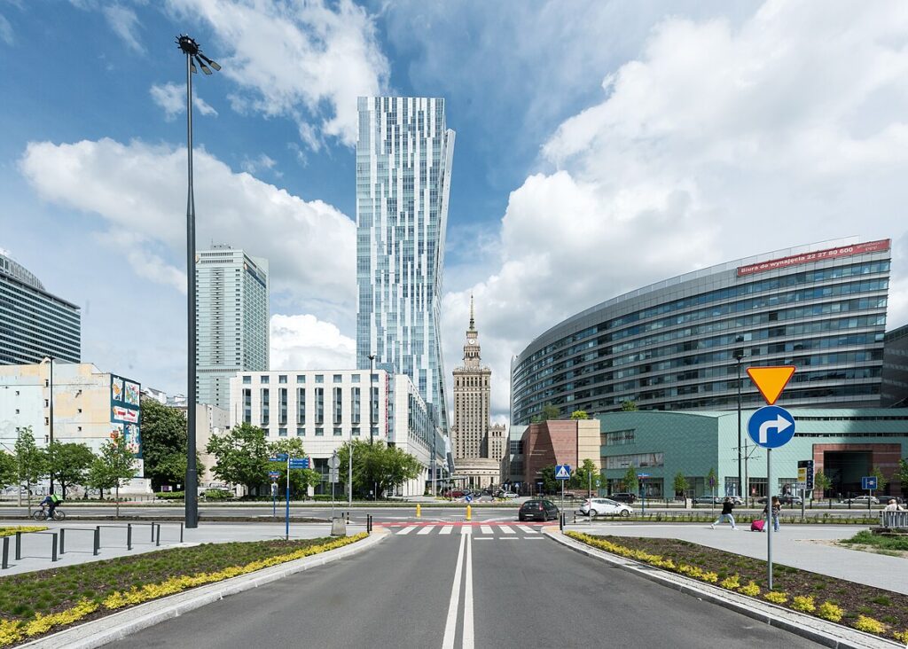 Nowoczesne wieżowce w centrum miasta, w tle widoczny zabytkowy budynek z wieżą, na drodze przejście dla pieszych.