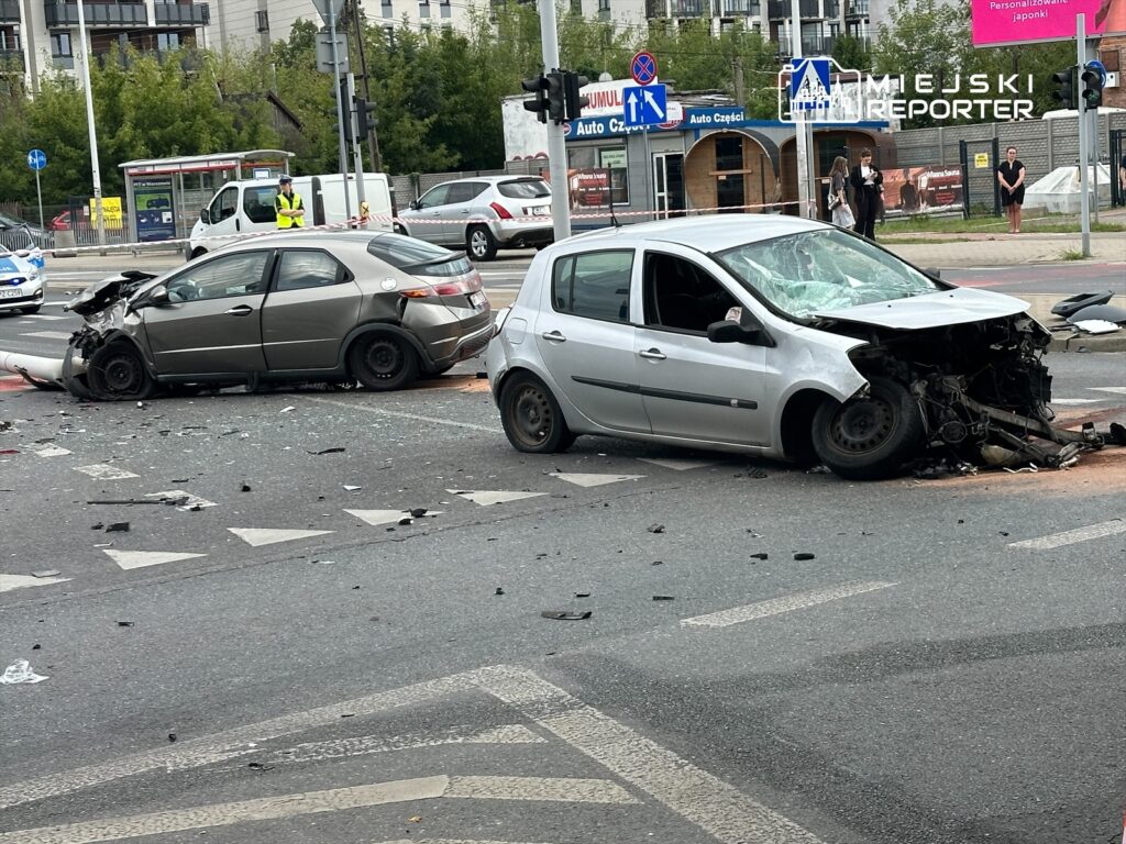 Dwa uszkodzone samochody osobowe na skrzyżowaniu, z rozrzuconymi fragmentami karoserii na jezdni.