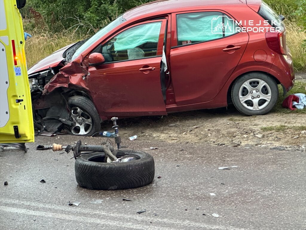 Czerwony samochód osobowy z uszkodzonym przodem stoi na poboczu drogi, obok leży oderwane koło.