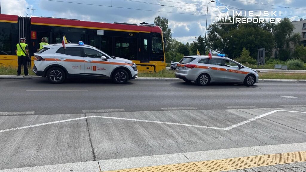 Funkcjonariusze w kamizelkach odblaskowych kontrolują ruch obok tramwaju na ulicy, obok zaparkowane pojazdy ZTM.