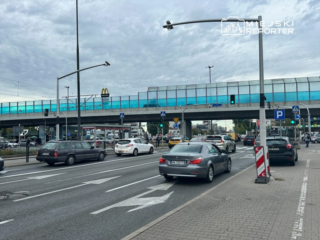 Ruch samochodowy na skrzyżowaniu z widocznym mostem i restauracją fast food w tle.
