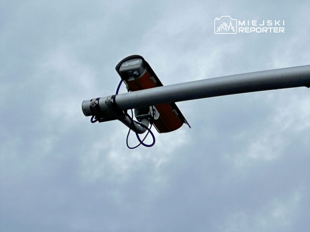 Kamera monitorująca zamontowana na stalowym słupie oświetleniowym, w tle pochmurne niebo.