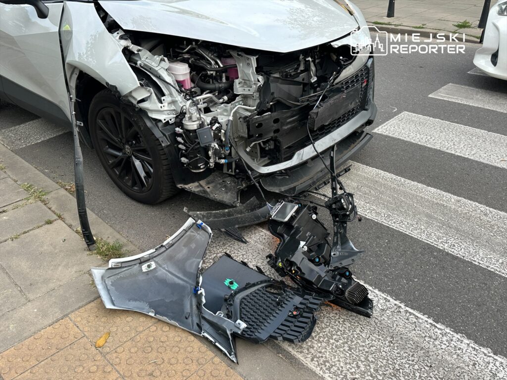 Uszkodzony samochód osobowy z zerwaną przednią częścią oraz częściami leżącymi na jezdni.