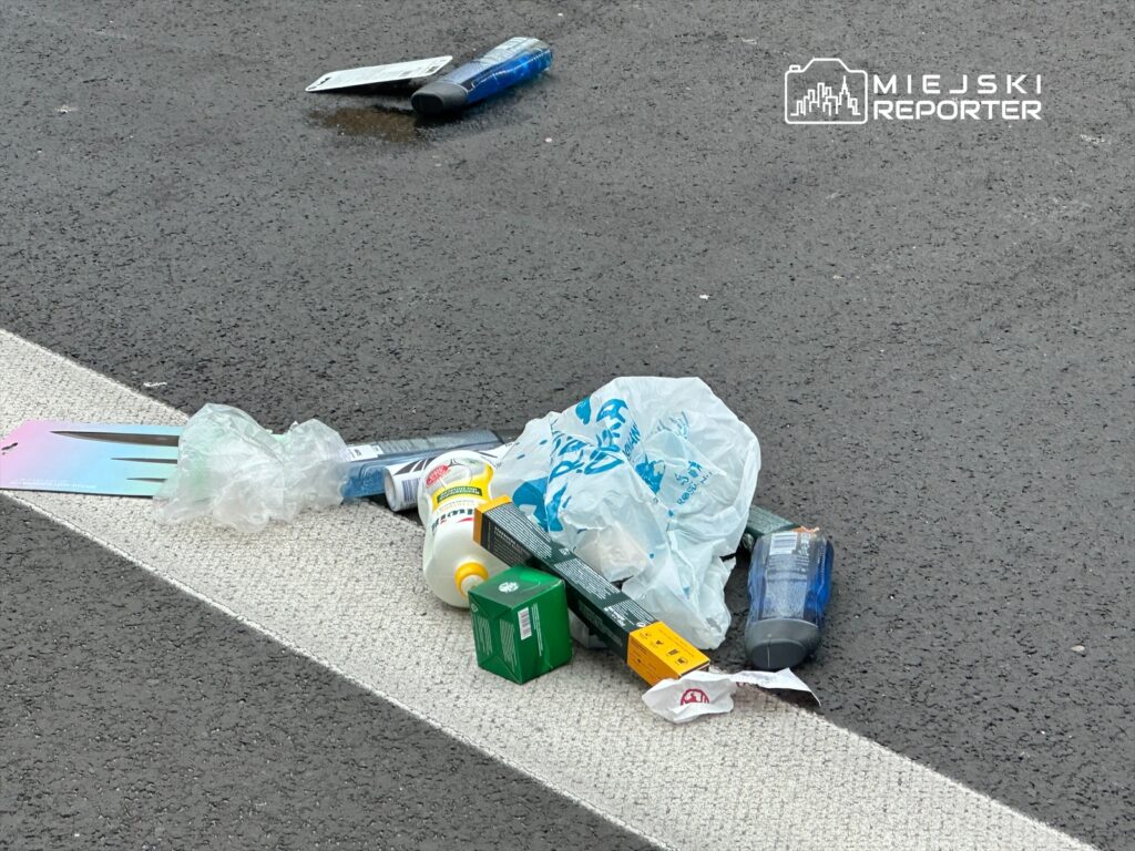 Odwiedzający pozostawili różnorodne odpady, w tym plastikowe torby i opakowania, na szarej nawierzchni drogi.
