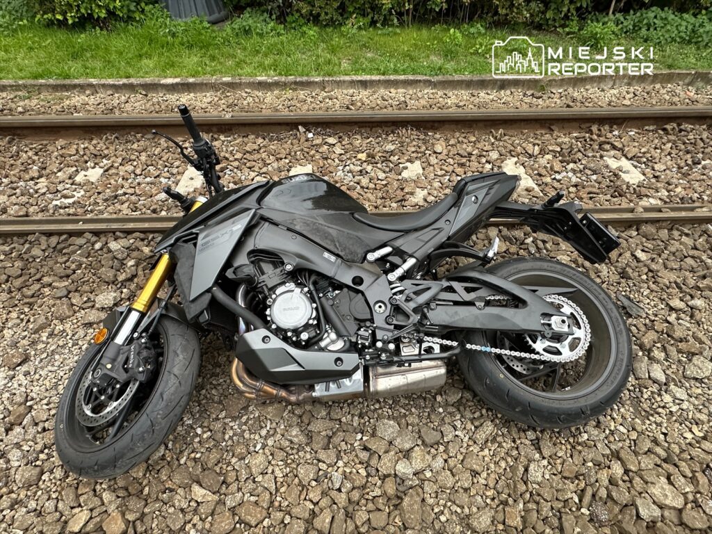 Uszkodzony motocykl leży na torach kolejowych, otoczony kamieniami i trawą.