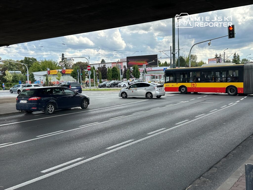 Ruchome pojazdy na skrzyżowaniu, w tle widoczny supermarket Biedronka oraz reklamy.