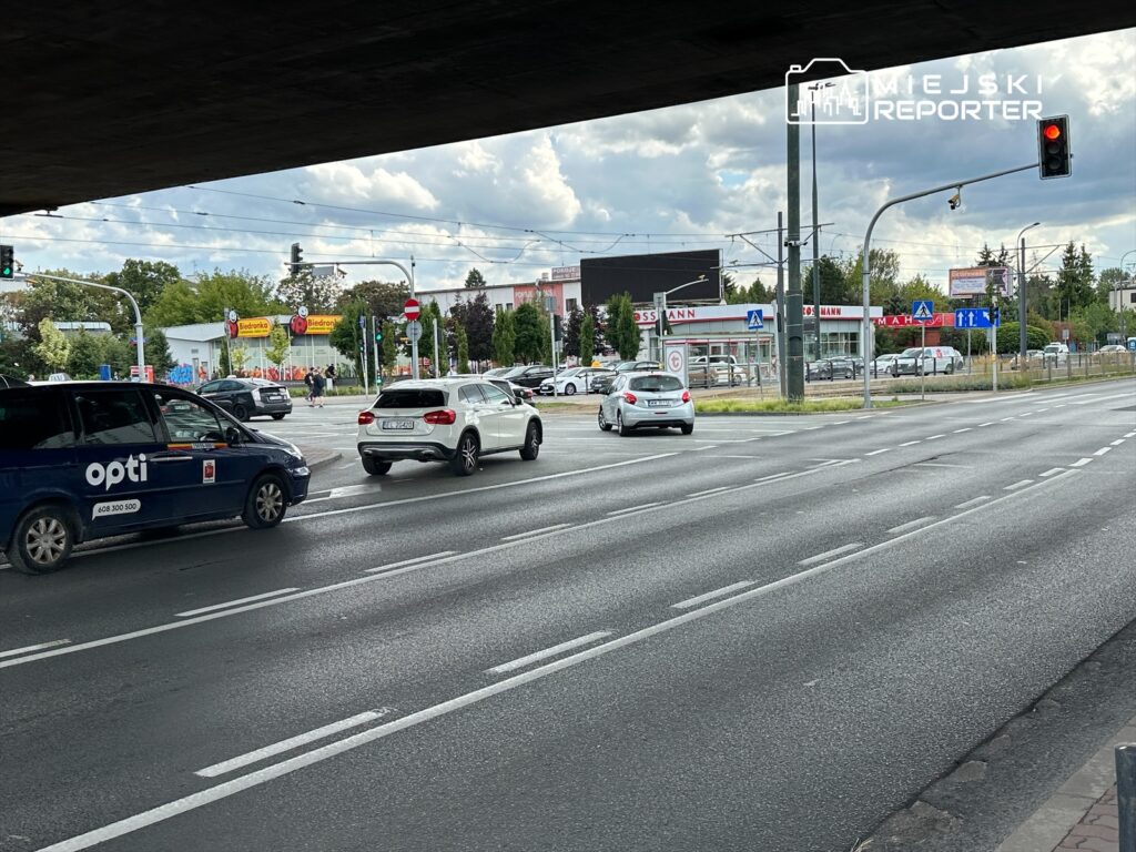 Ruch samochodowy na skrzyżowaniu z sygnalizacją świetlną, w tle widoczny sklep Biedronka oraz inne budynki.