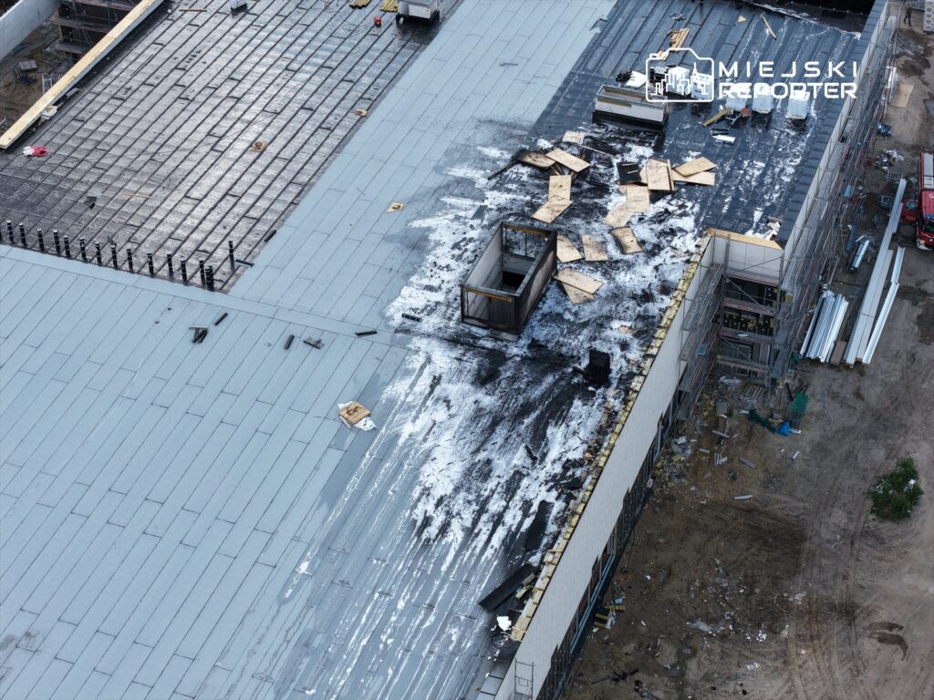Nowy budynek w trakcie budowy z widocznym dachem pokrytym materiałami budowlanymi i fragmentami drewna.