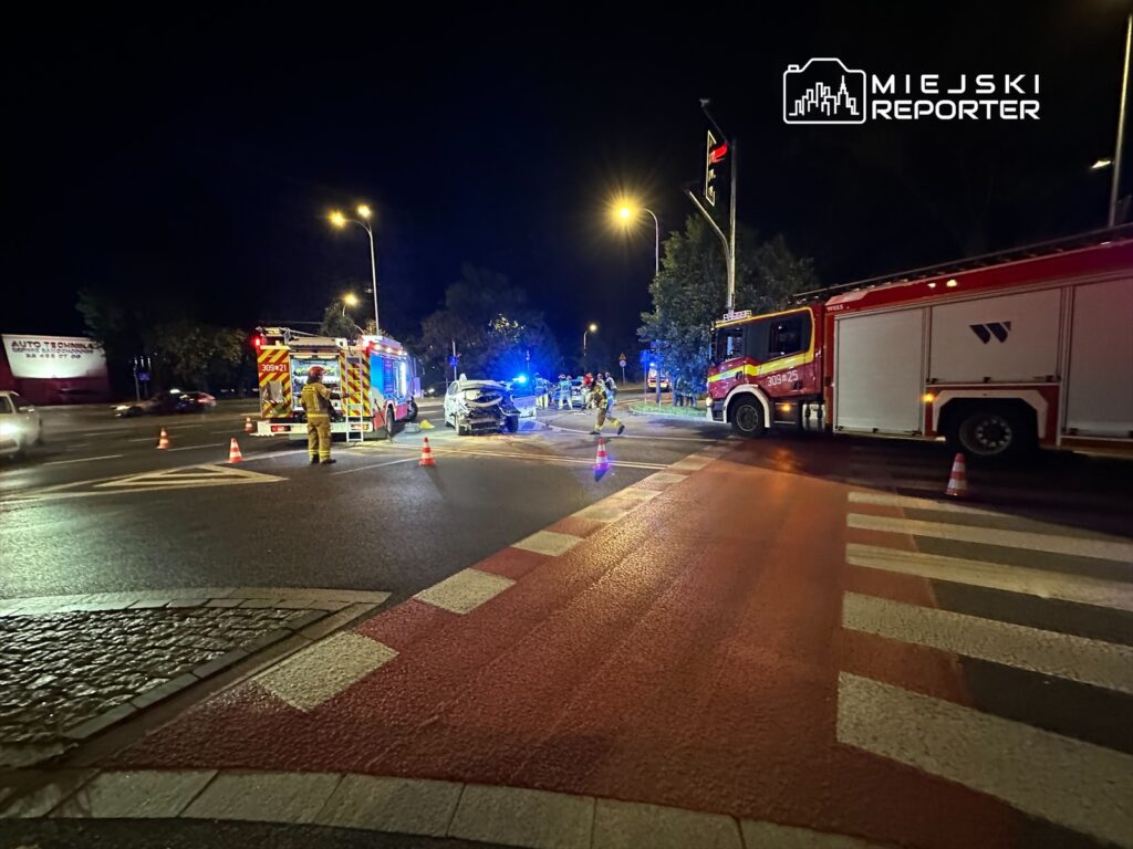 Na skrzyżowaniu ulic, strażacy i służby ratunkowe pracują przy wypadku drogowym w nocy.