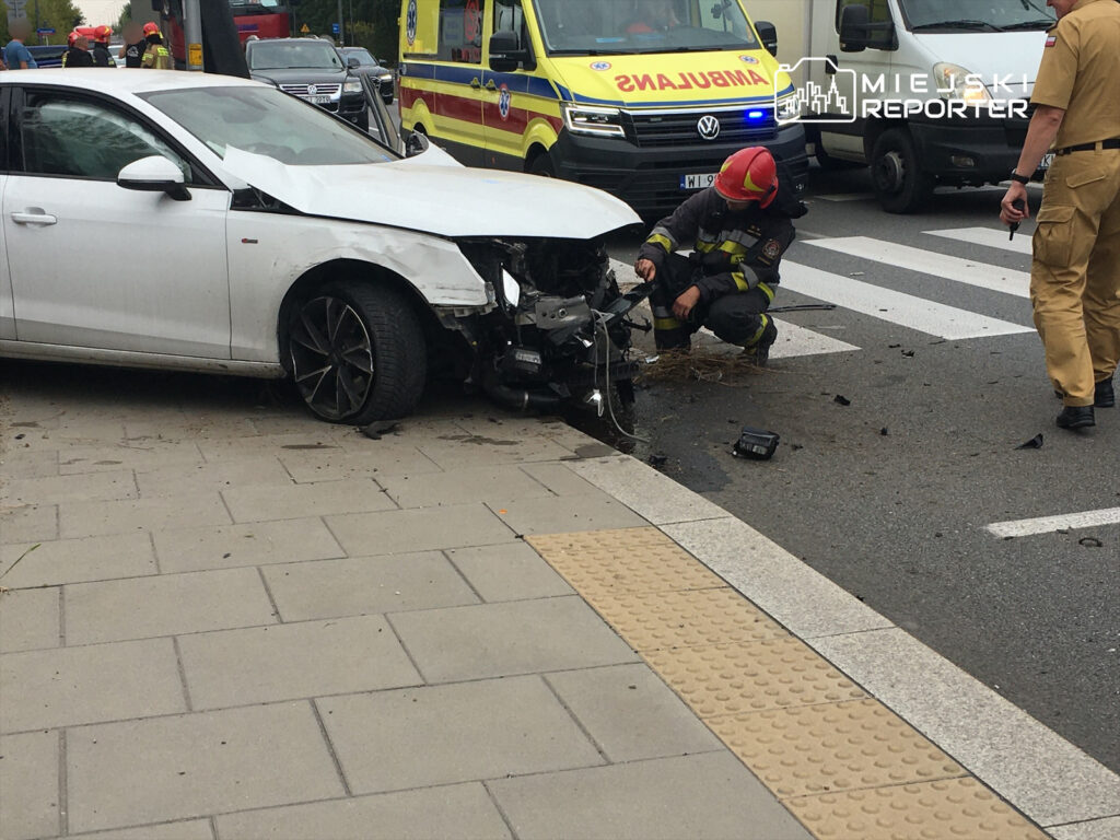 Strażak sprawdzający uszkodzenia białego samochodu osobowego po wypadku drogowym na ulicy w mieście.