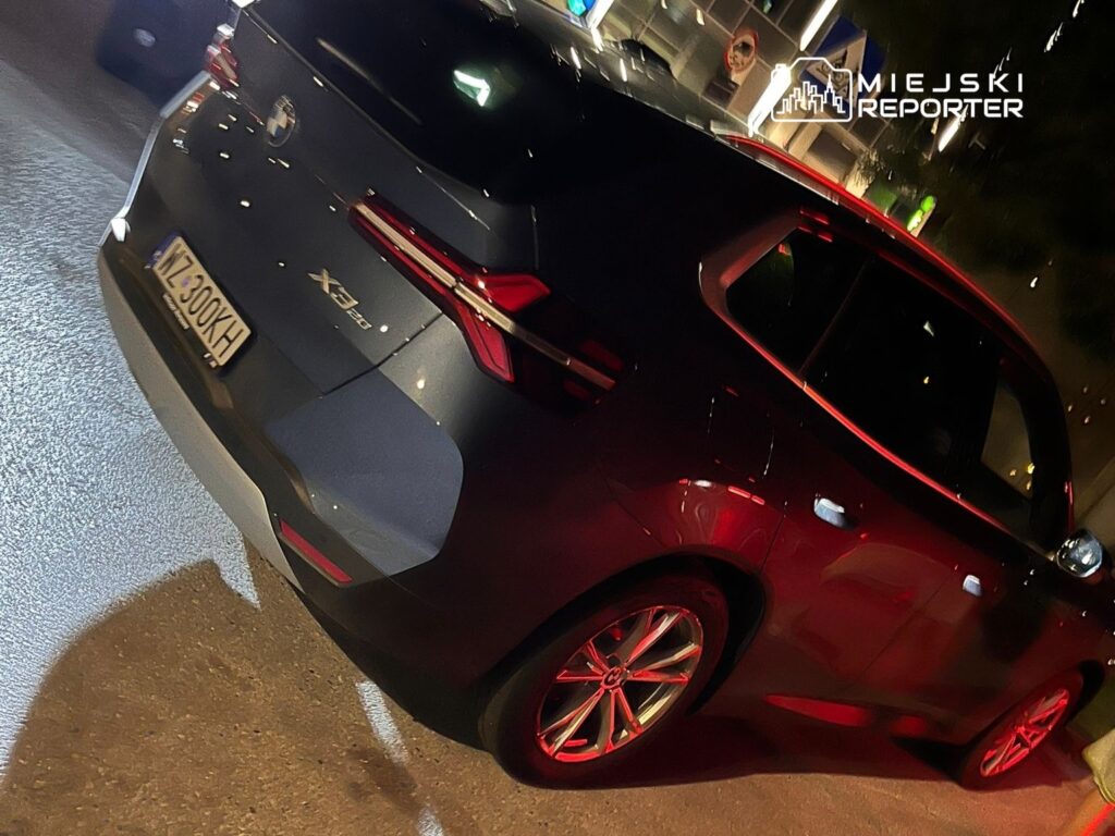 Nowoczesny SUV w kolorze ciemnoszarym, z podświetleniem tylnych lamp, zaparkowany na oświetlonym parkingu.