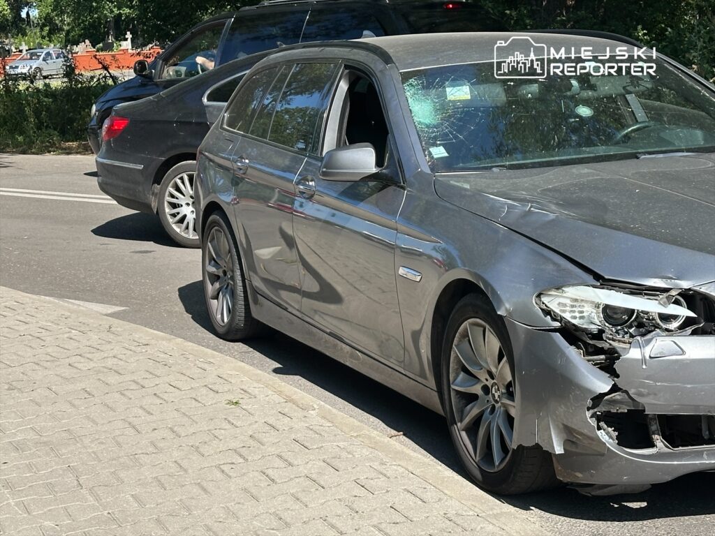 Uszkodzony srebrny samochód osobowy zaparkowany na ulicy, z wybitym oknem i uszkodzoną przednią częścią.