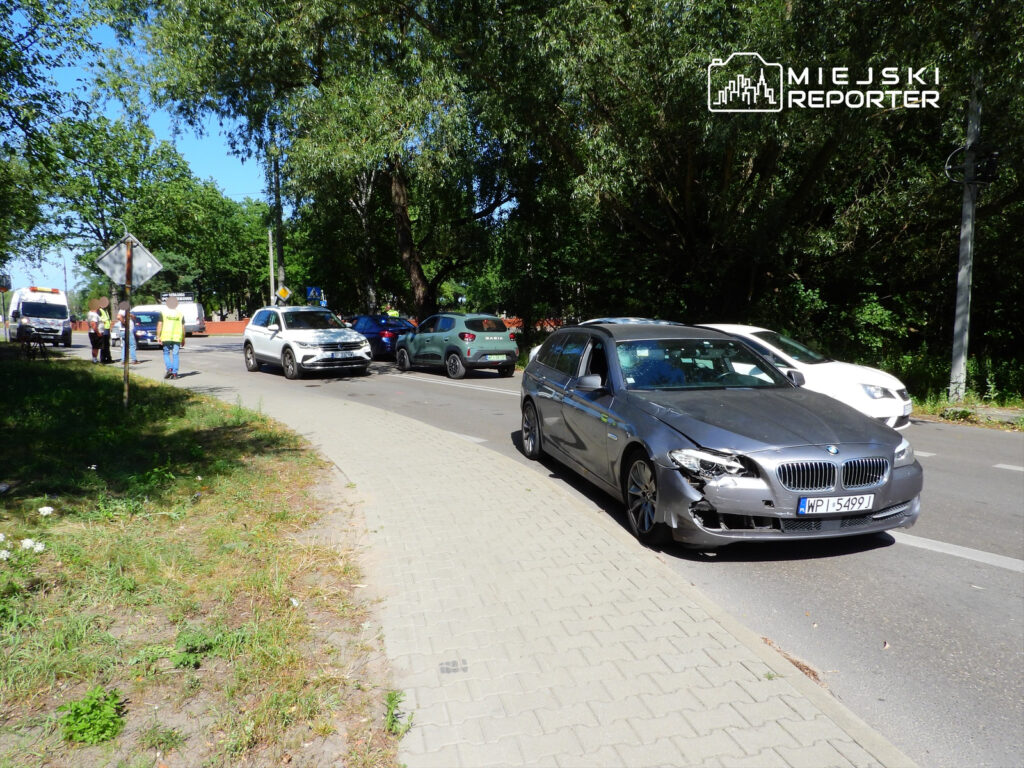 Na jezdni stoi uszkodzony samochód osobowy, obok pracują funkcjonariusze w kamizelkach odblaskowych.