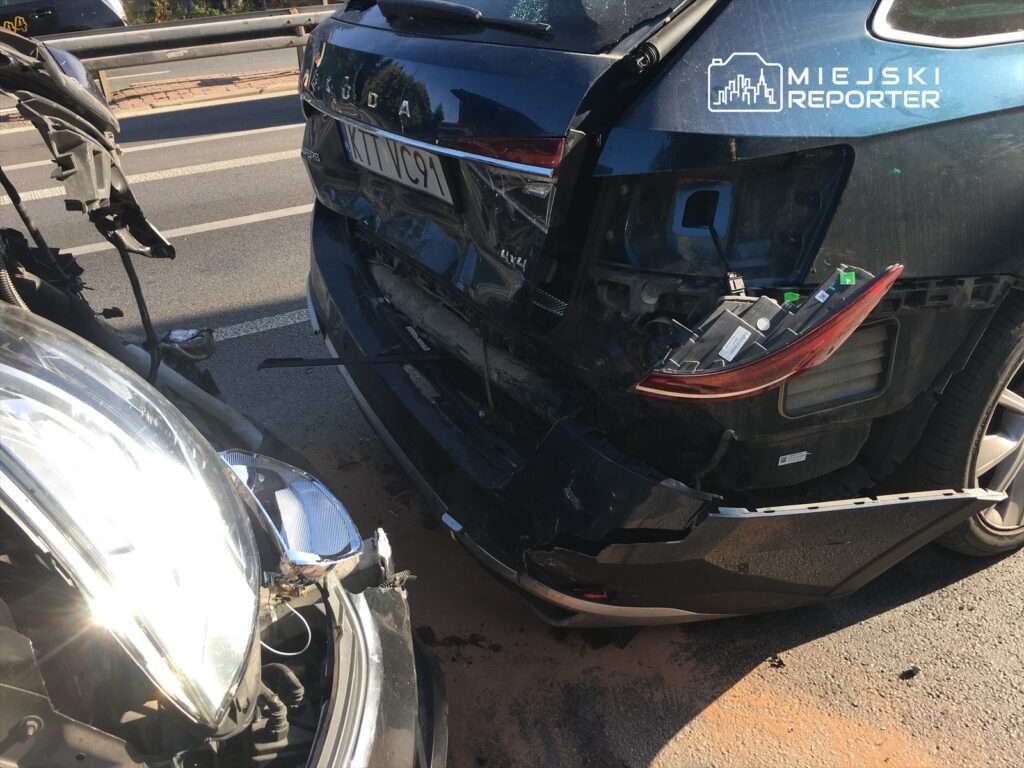 Zderzenie dwóch samochodów na drodze, z uszkodzoną przednią częścią jednego i tylną częścią drugiego.