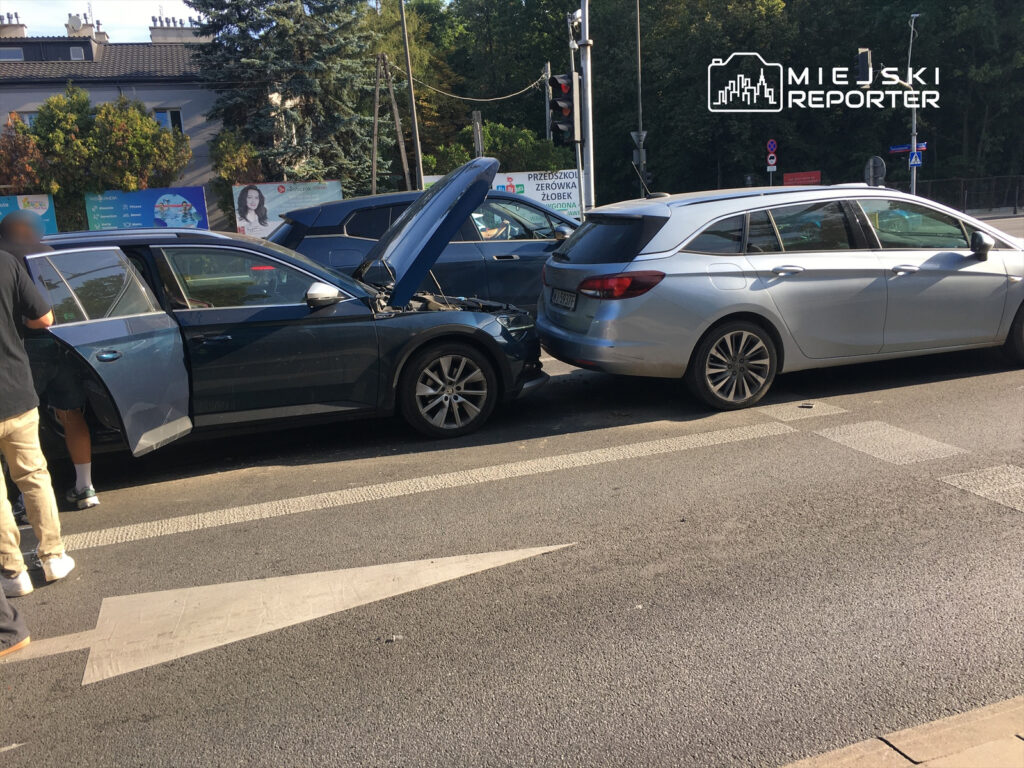 Mężczyzna w czarnej koszulce sprawdza uszkodzenia dwóch samochodów po kolizji na ruchliwej ulicy.