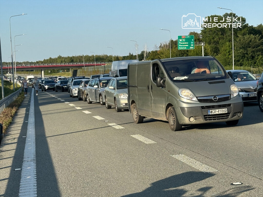 Kierowca dostawczego samochodu stojącego w korku na autostradzie, obok ruchu samochodowego w stronę miasta.