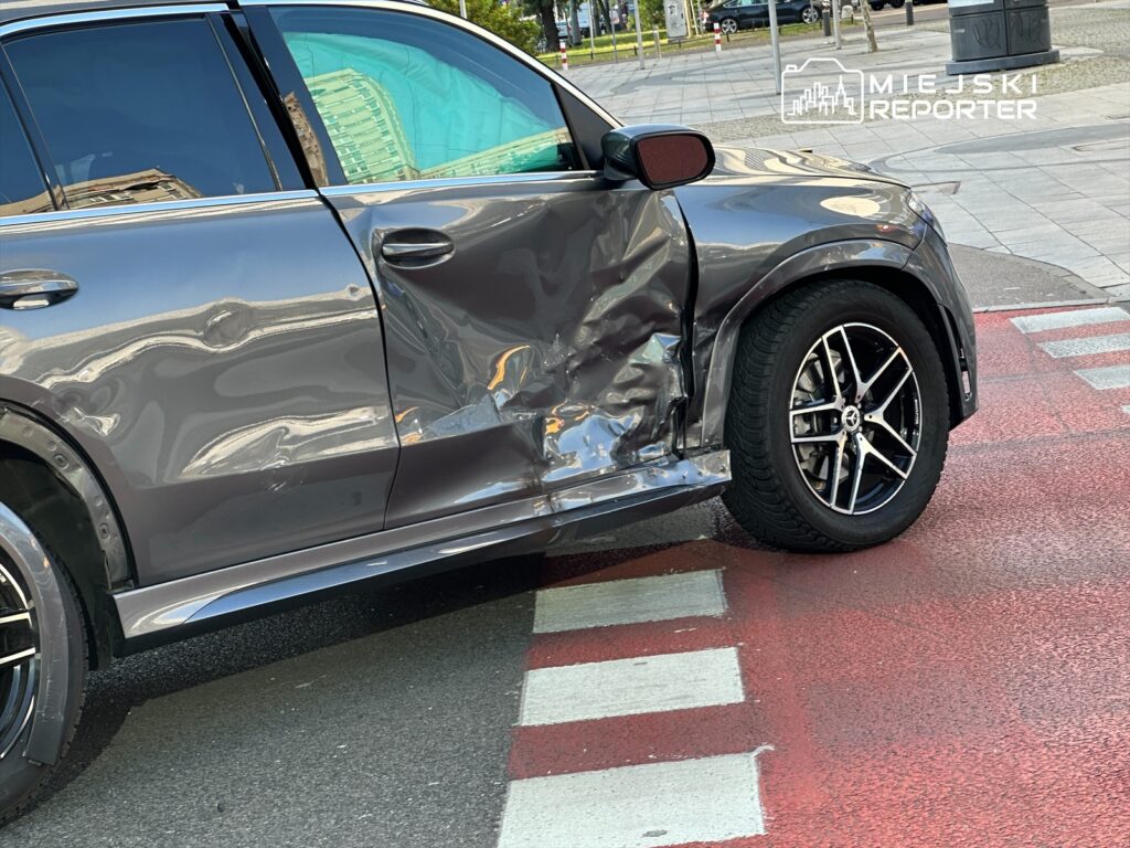Uszkodzony samochód osobowy stojący na przejściu dla pieszych z widoczną wgniecioną karoserią.